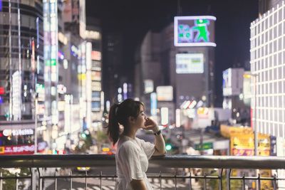 Woman standing by illuminated buildings in city at night