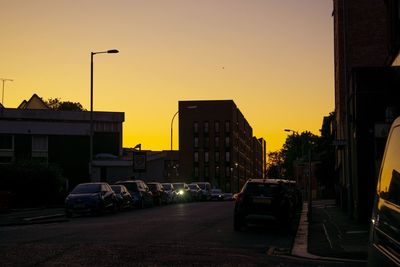 Cars on street by buildings against sky during sunset