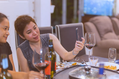 Selected focus two woman with red wine on table having video call on smart phone.