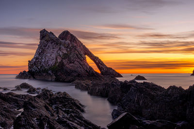 Rock formation in sea against sky during sunset