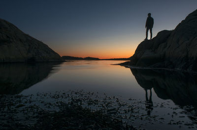 Silhouette people standing on rock by lake against sky during sunset