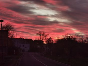 Road by trees against sky during sunset