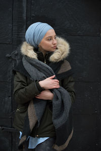 Young woman wearing warm clothing while looking away against wall in winter