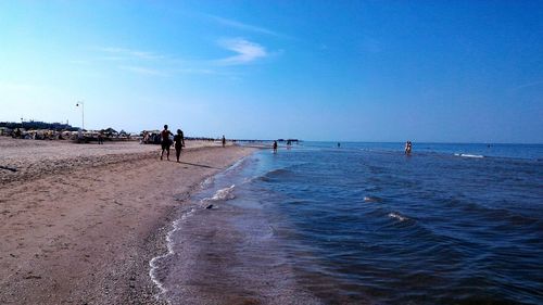 People walking on beach against clear blue sky