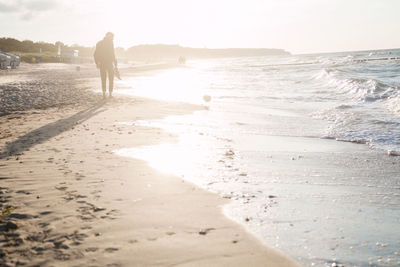 Man walking on beach against sky during sunset