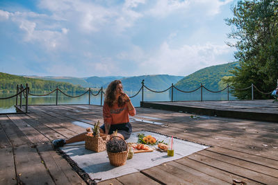 Young woman sitting in picnic blanket on pier