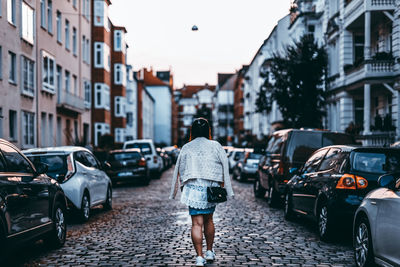 Rear view of woman walking on street in city between cars