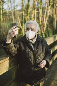 Elderly woman taking selfie through mobile phone while standing on footbridge during covid-19