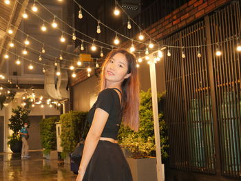 Portrait of young woman standing against illuminated christmas tree