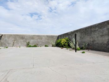 View of concrete wall with building against cloudy sky