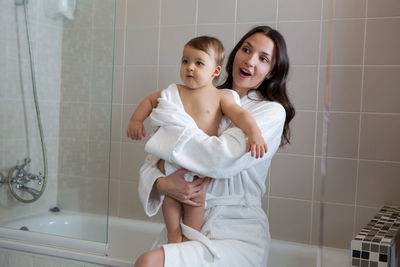 Mother in a bathrobe and with a child standing in the bathroom