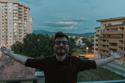 Young man at city balcony enjoying town view with open arms on a beatiful day of summer