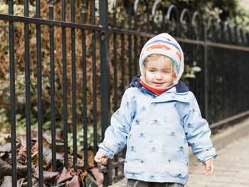 Portrait of baby girl wearing warm clothing while standing against fence