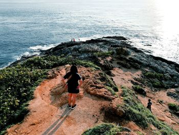 Rear view of woman walking on rock by sea