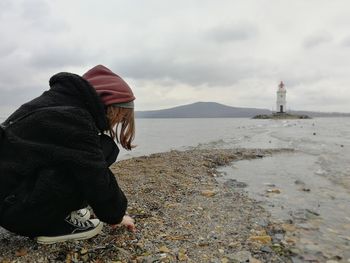 Girl in hood sitting by the sea