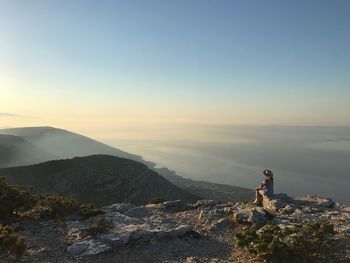 Rear view of woman standing on rock against sky