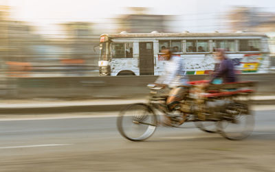Blurred motion of man riding bicycle against bus on road in city