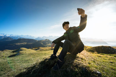 Man taking selfie through mobile phone on field against sky