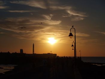 Silhouette street light by sea against sky during sunset