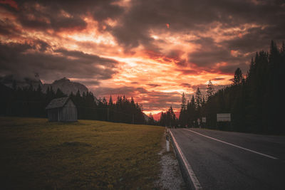 Road by trees against sky during sunset