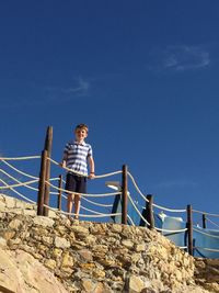 Low angle view of boy standing against clear blue sky