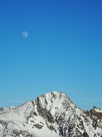 Low angle view of snowcapped mountains against clear blue sky