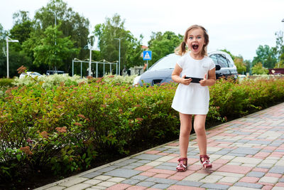 Portrait of surprised girl holding mobile phone on footpath
