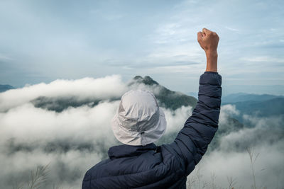 Rear view of person with arms raised looking at landscape against cloudy sky