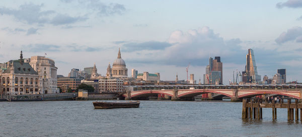 Bridge over river in city against cloudy sky