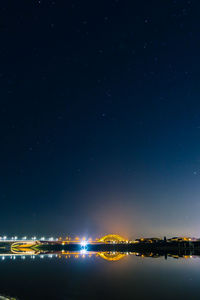 Illuminated city by sea against sky at night