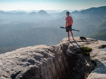 Barefoot man in red t-shirt stay with tripod on rock. saxony switzerland, grosser zschand valley.