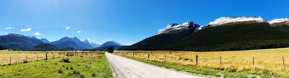 Road amidst field and mountains against blue sky