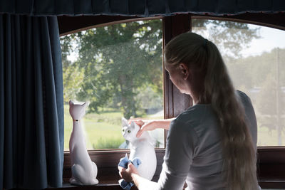 Woman wipes a porcelain figurine of a white cat on the windowsill,room cleaning