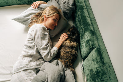 A woman in the morning after waking up lies in bed and pets a domestic cat.