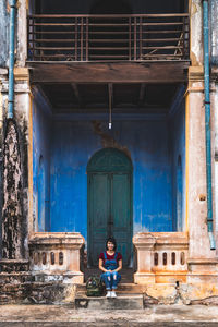 Full length of woman sitting against old house