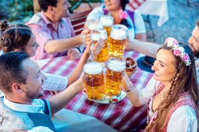 High angle view of friends toasting beer while sitting at restaurant