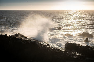 Waves splashing on rocks at shore against sky