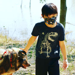 Boy wearing mask with dog while standing outdoors