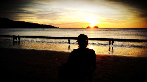 Rear view of silhouette woman standing at beach during sunset