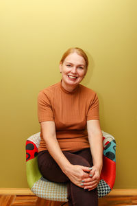 Portrait of young woman sitting against yellow background