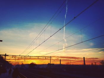 Silhouette electricity pylons against sky during sunset