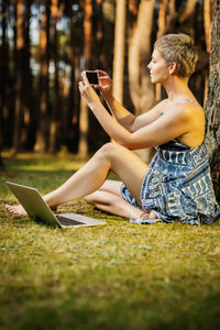 Woman photographing through camera while sitting on field