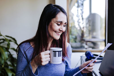 Happy woman with coffee cup holding sheet