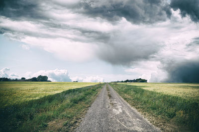 Empty road amidst field against sky