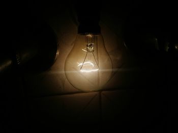 Low angle view of illuminated light bulb hanging at night