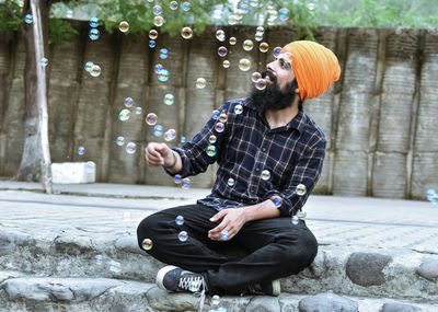 Full length of man wearing turban sitting by bubbles