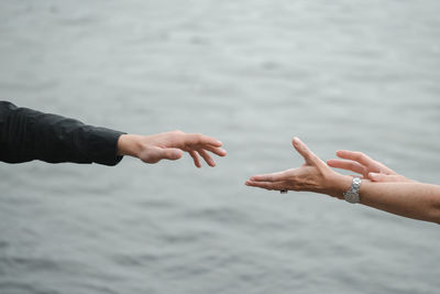 Man and woman hands reaching out each other, holding hands over grey monochrome water. relations