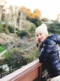 Portrait of smiling young woman in warm clothing leaning on railing