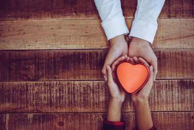 Cropped hands of couple holding heart shape decoration over table