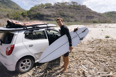 Young man with surfboard near car